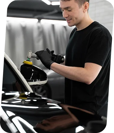 Especialista em estética automóvel polindo um espelho retrovisor com ferramentas de precisão em uma oficina profissional de detalhamento.