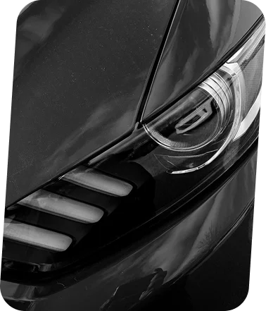 Foto monocromática em close-up de um farol de carro que destaca linhas nítidas, superfícies reflexivas e o design moderno do veículo.